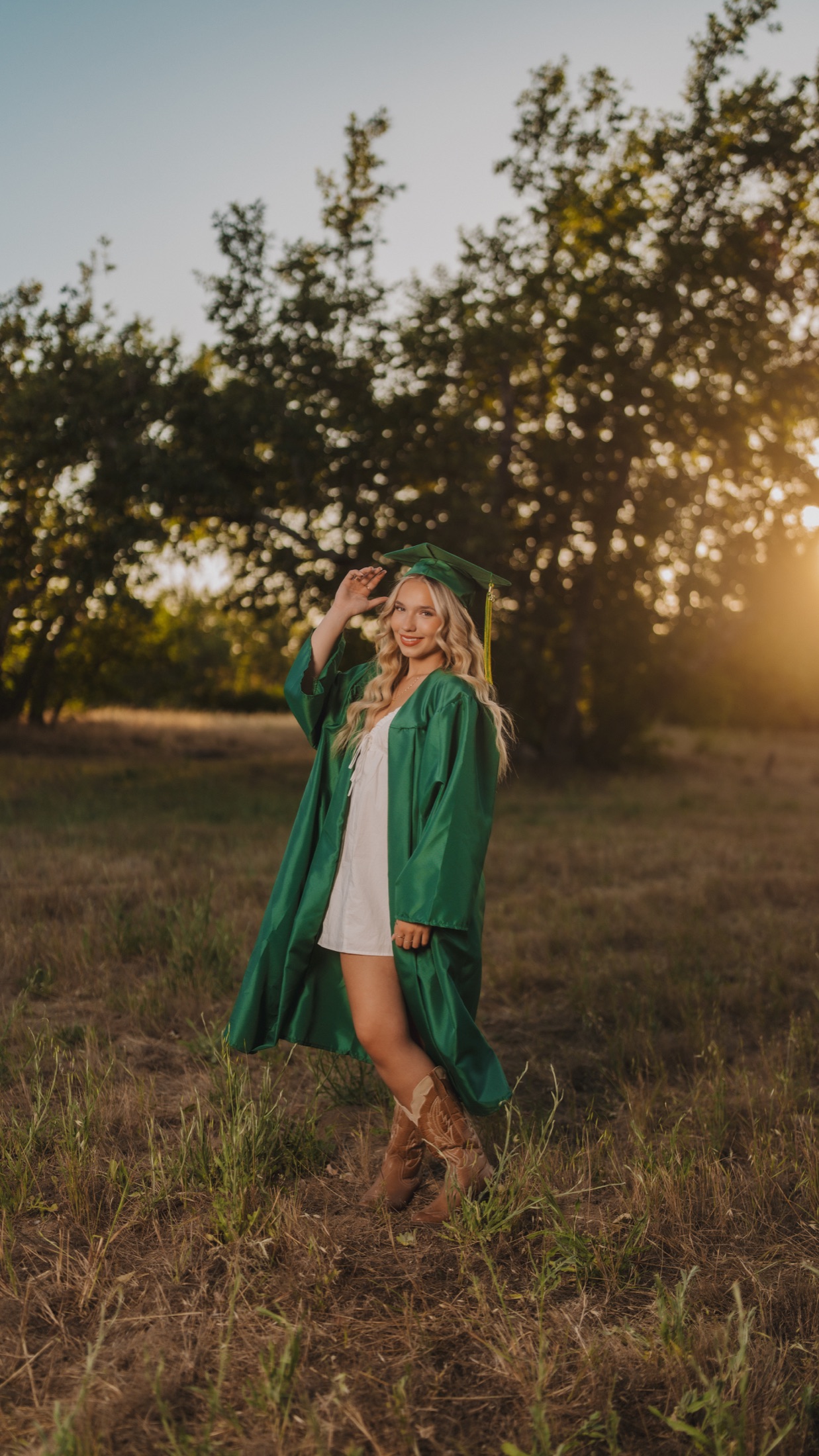 Senior in a green graduation cap and gown at golden hour